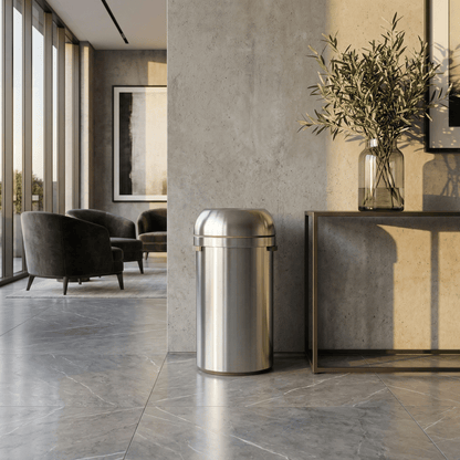Simplehuman's 60L All-Steel Bullet Open Can in Brushed in a modern living room or lobby setting with floor to ceiling windows, mood lighting, plants, and a few paintings in the background.