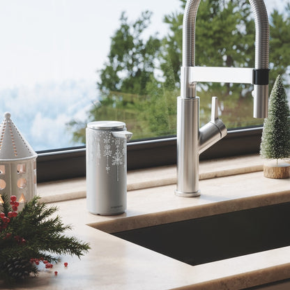 Lifestyle view of Simplehuman Silver Metallic 2024 Holiday Sleeve (9 oz.) in a winter kitchen setting, snowflake design.